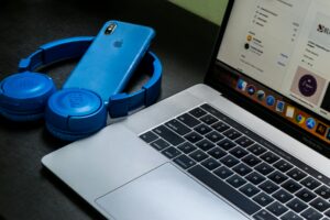 A sleek office setup featuring a laptop, blue headphones, and a smartphone, exemplifying modern technology.