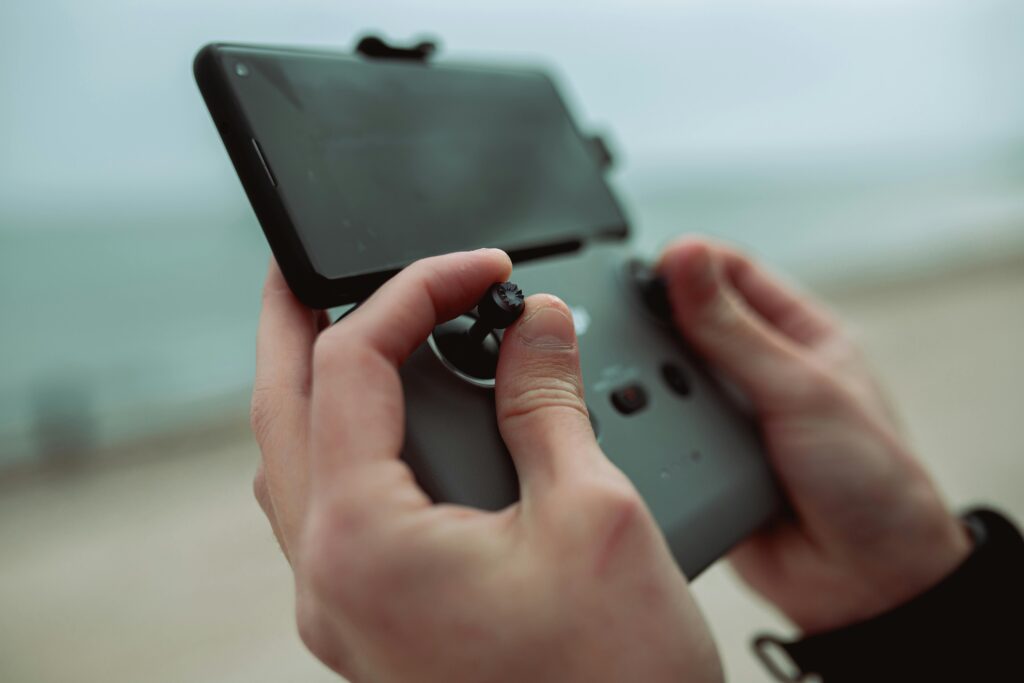 Close-up of hands operating a drone controller with smartphone by the ocean.