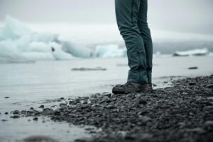 A person standing on a rocky shore with icebergs in the background in Reykjanesbær, Iceland.
