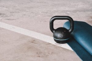 Kettlebell and blue yoga mat on a concrete floor in an indoor gym setting.