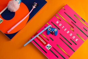 Vibrant photo of school supplies featuring colorful notebooks and pens on an orange backdrop.