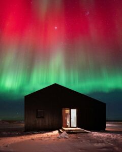 Stunning view of Northern Lights over a snowy cabin in Iceland's winter night.