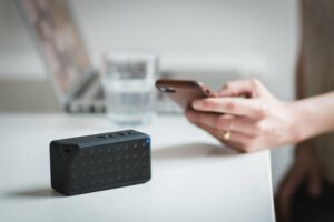 Person connecting a smartphone to a wireless speaker indoors, foreground focus.