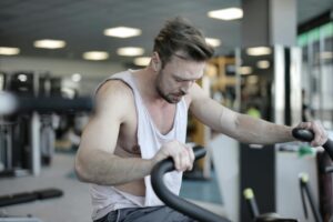 Exhausted male athlete with muscles training on exercise machine and working on endurance in modern sports center