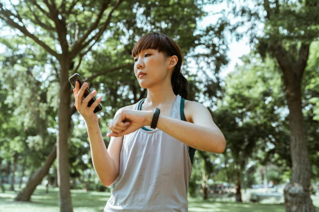 Young Asian woman checking her fitness tracker on a sunny day in the park, staying active and healthy.