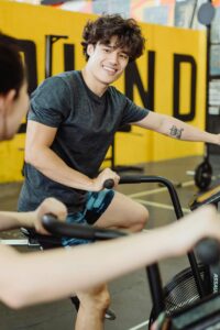 A cheerful Asian man exercising on a stationary bike indoors, promoting fitness and happiness.