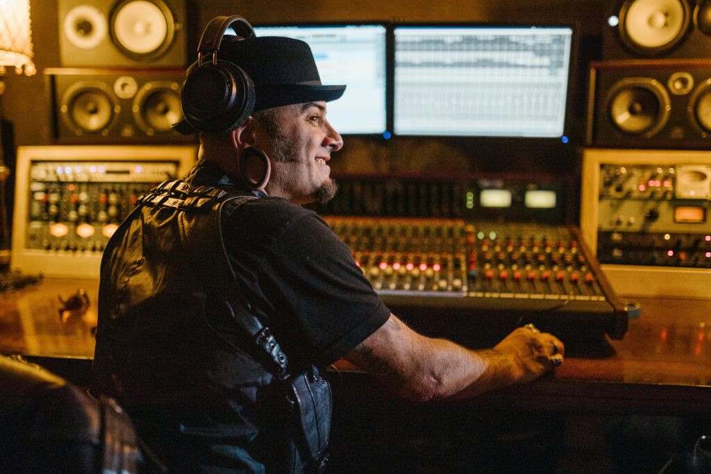 A person working in a recording studio wearing headphones and a hat, using audio equipment.