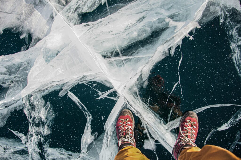 A close-up view of red hiking boots standing on a cracked ice surface, showing intricate ice patterns.
