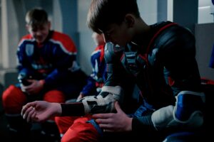 Teenage hockey players donning gear in the dressing room before a match.