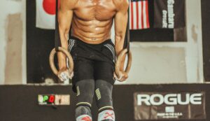 Strong athlete doing ring workout in a gym, showcasing muscular physique and strength training.