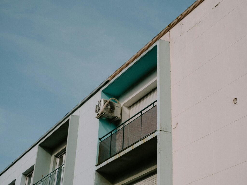 A low angle view of a modern apartment building featuring a balcony and air conditioner unit.