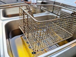 Close-up of a stainless steel fryer basket over hot cooking oil, emphasizing the metal craftsmanship.