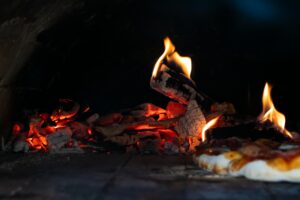 Close-up view of a wood-fired pizza oven with embers and a freshly baked pizza.
