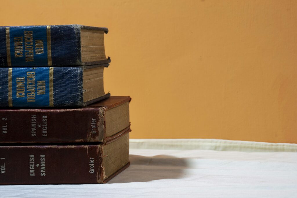A close-up of vintage English-Spanish dictionaries stacked on a table against a warm backdrop.