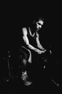 Black and white portrait of an adult male exerting effort on an indoor stationary bike.