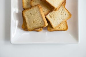 Stack of toasted bread slices on a white ceramic plate, perfect for breakfast or snacks.