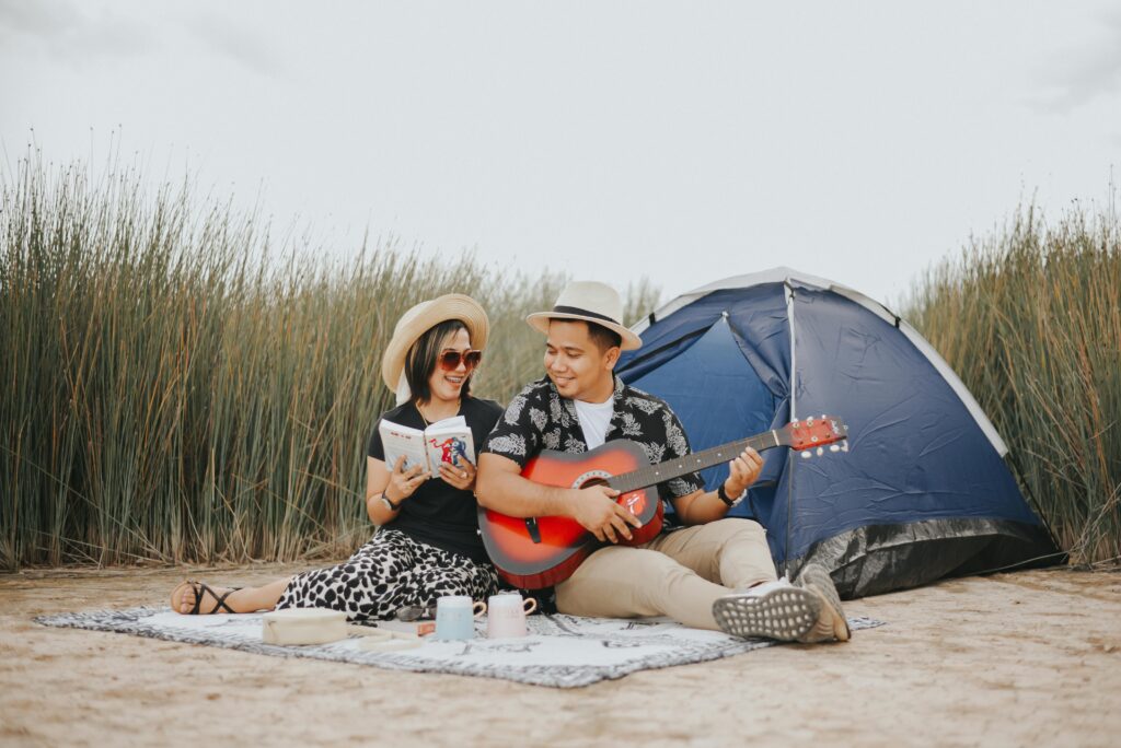 A cheerful couple having a picnic with guitar music and book under the open sky.