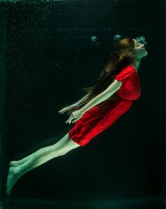 A woman in a red dress gracefully floats underwater, capturing a dreamlike essence.