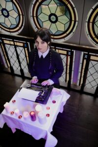 A woman in gothic attire sits at a typewriter surrounded by candles, evoking a vintage, mysterious atmosphere.
