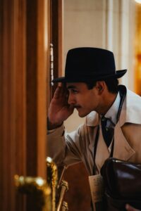 A man in a vintage suit and hat peeks through a doorway inside a stylish setting, exuding a classic fashion vibe.