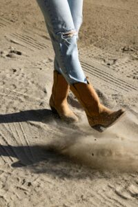 Close-up of legs in jeans and cowgirl boots kicking up dust in Temecula, CA.