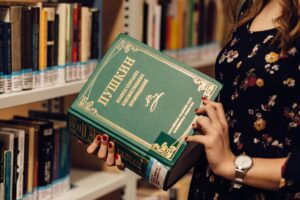 A woman holds a Russian literature book in a library, showcasing a focused study environment.