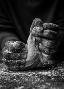 Artistic black and white photo of hands kneading dough, showcasing texture and craftsmanship.