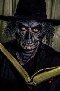 Close-up of a person in skeleton makeup holding an open book, creating a spooky atmosphere.