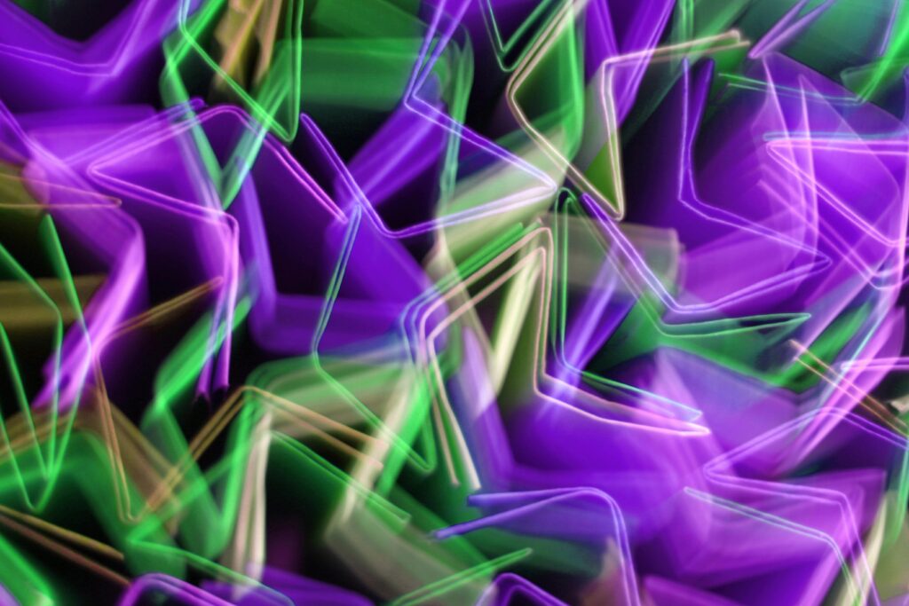 Dynamic abstract image featuring vivid purple and green light trails in motion.