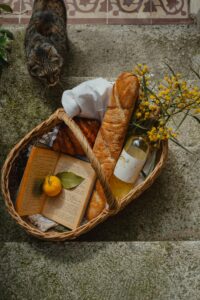 Basket featuring a baguette, book, wine, and cat, evokes a rustic outdoor vibe.