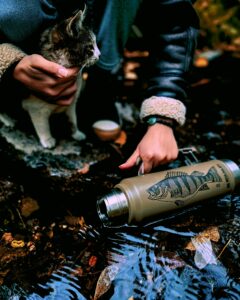 Outdoor scene of person holding cat near a stream with a thermos in Eskişehir, Türkiye.