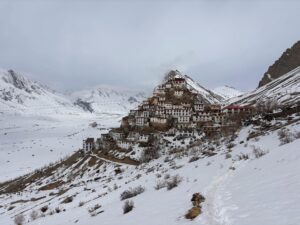 A breathtaking view of Key Monastery nestled in the snow-covered Himalayas under a cloudy sky.