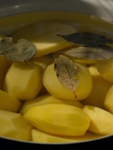 Close-up of peeled potatoes submerged in water with bay leaves.