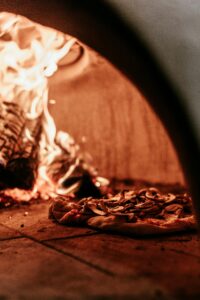 Close-up of a pizza baking in an authentic wood-fired oven, showcasing flames and rustic ambiance.