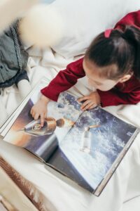 Young girl exploring a space-themed book indoors, capturing curiosity and enjoyment.