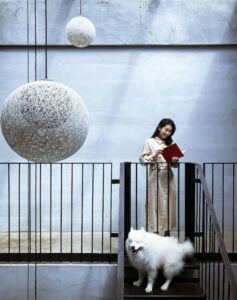 Woman reading a book on stairs with a Samoyed dog in a modern interior.