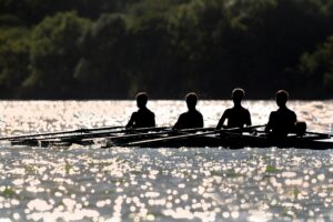 Silhouetted rowers paddle on a shimmering lake under vibrant sunlight.