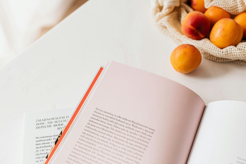 From above of opened book placed on white table near cotton sack with natural ripe apricots