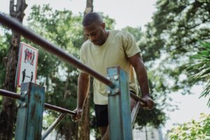 Adult man performing dip exercise on parallel bars outdoors in a park setting.
