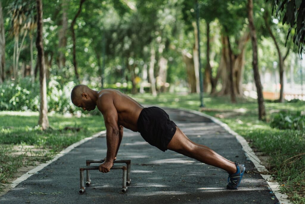 Man performing push-ups on parallel bars in a park, showcasing fitness and strength.