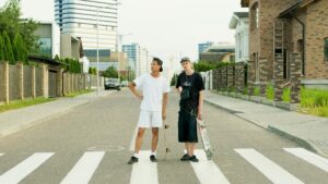 Two young skateboarders standing confidently on a city street crosswalk.