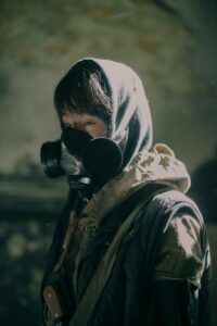 Moody portrait of a person wearing a gas mask and hood in a dystopian setting.