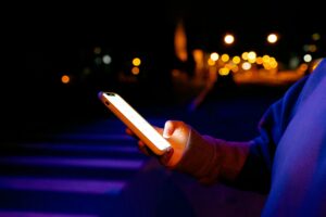 A person holds a glowing smartphone outdoors at night with bokeh lights in the background.