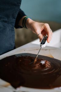 A baker using a digital thermometer to check the temperature of melted chocolate.