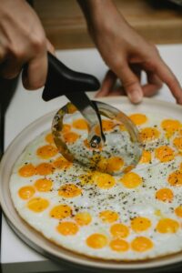 High angle crop anonymous cook slicing yummy fried quail eggs with pizza cutter in kitchen