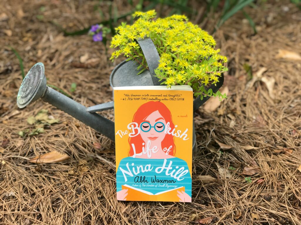 A vibrant book cover displayed with a watering can and plants in a garden setting.