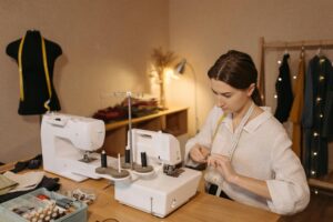 Caucasian woman threading a sewing machine in a fashion workshop. Focused and creative environment.