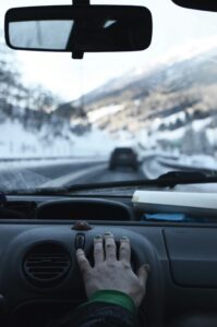Driving through snowy mountains in winter. Hand on car air vent. Road trip experience.