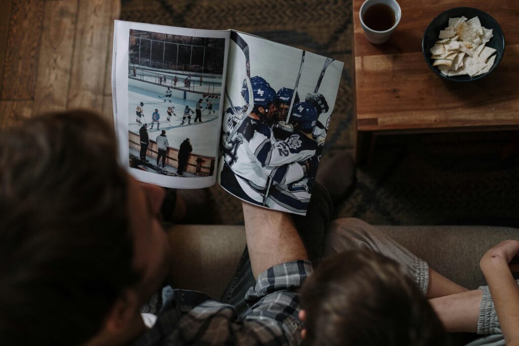 A cozy moment with a father and child reading a hockey magazine together indoors.