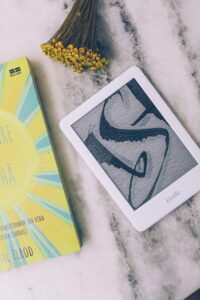 Flat lay of a Kindle and book on marble with flowers.